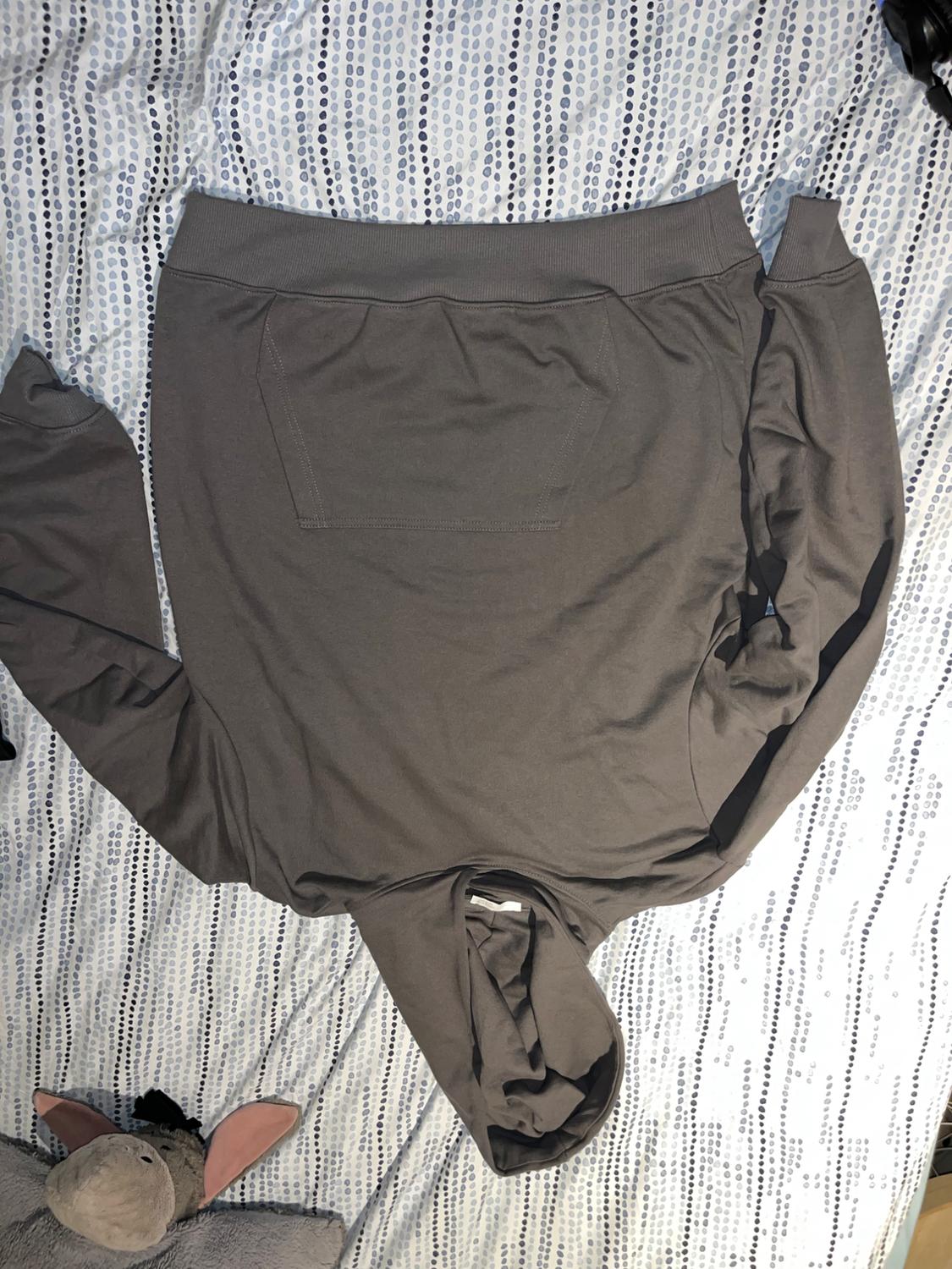 Grey hoodie with a front pocket, placed on a bed with blue and white polka dot sheets. Grey soft toy next to it.