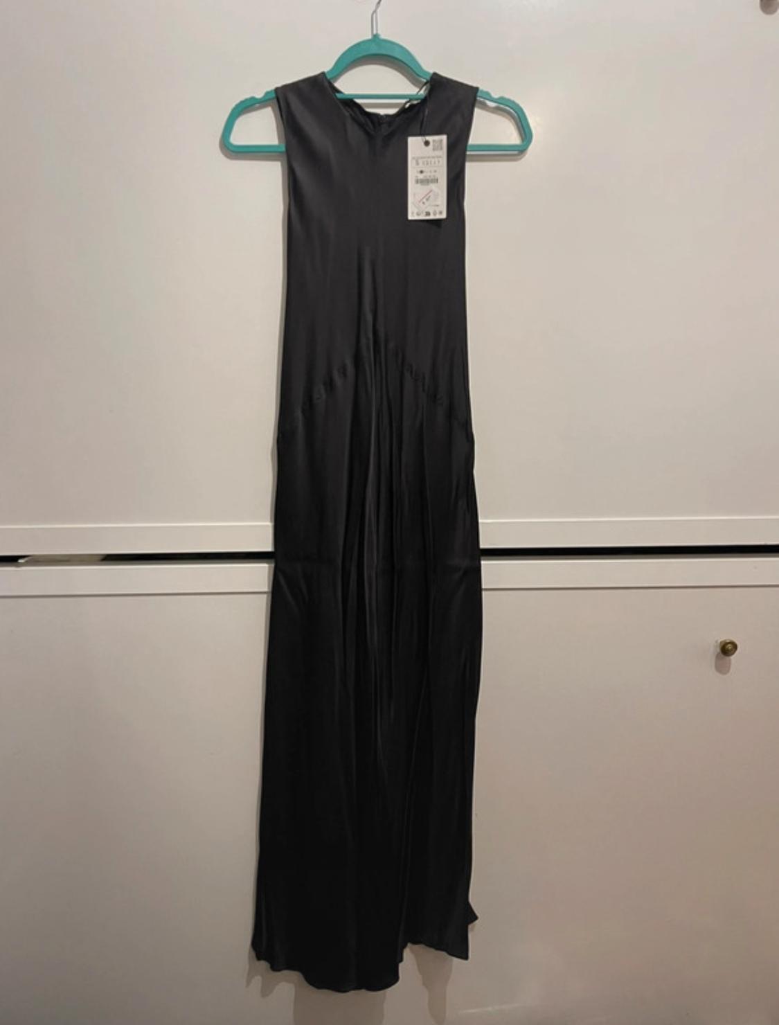 Sleeveless black dress hanging on a green hanger, with visible label on a white background.