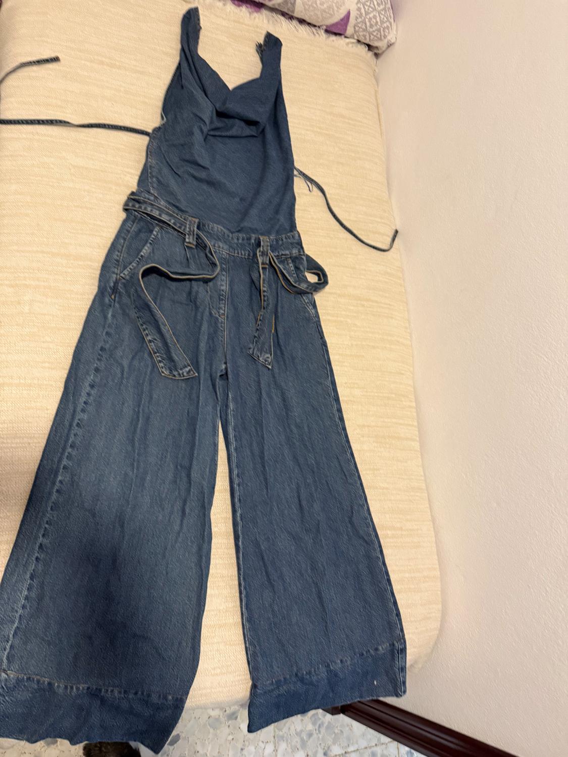 Blue wide-leg denim dungarees with straps and a matching belt, laid out on a light surface in a casual home setting.