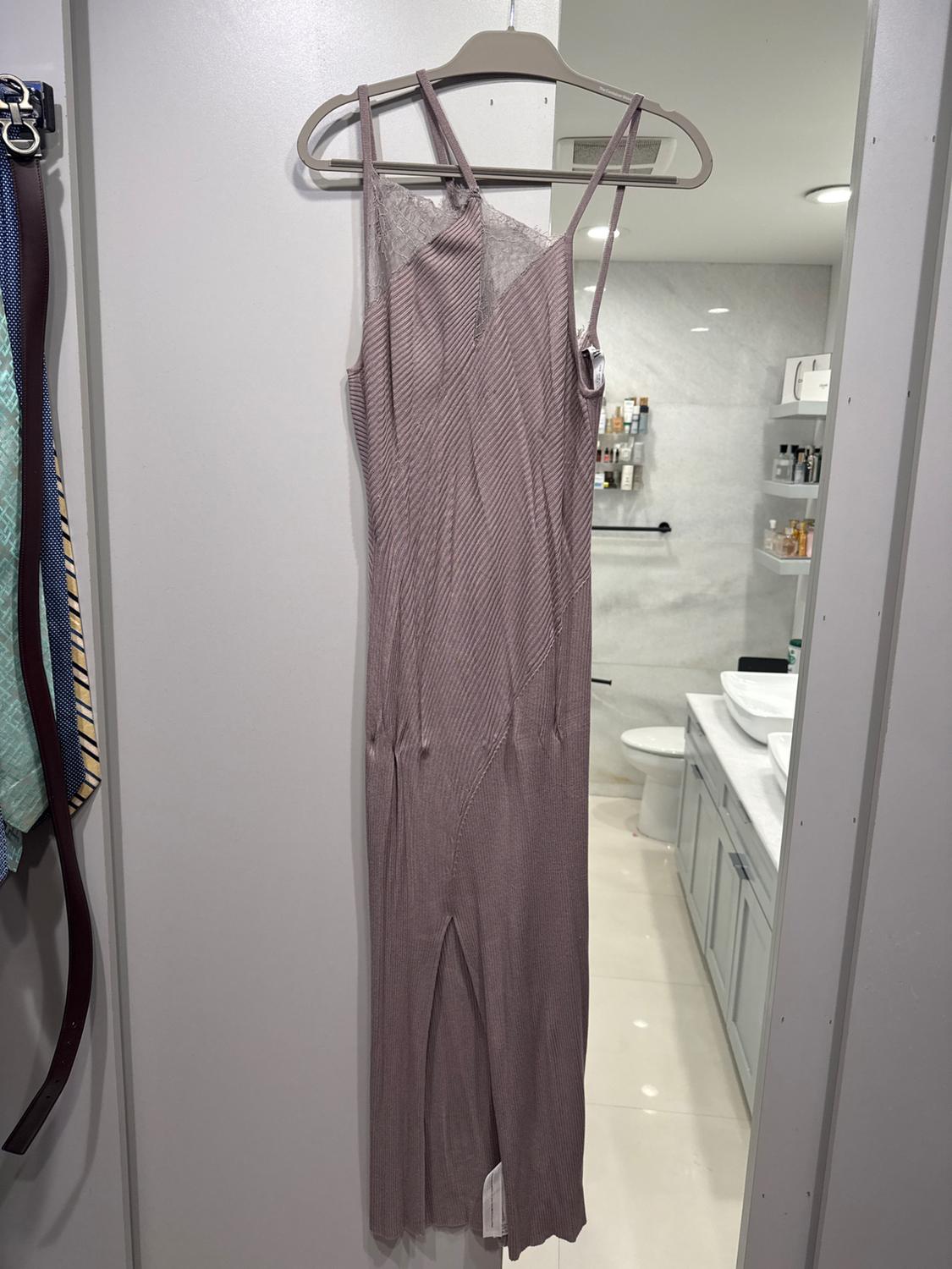 Long dress with spaghetti straps and lace hung on a hanger in a modern bathroom with white walls and shelves with products.