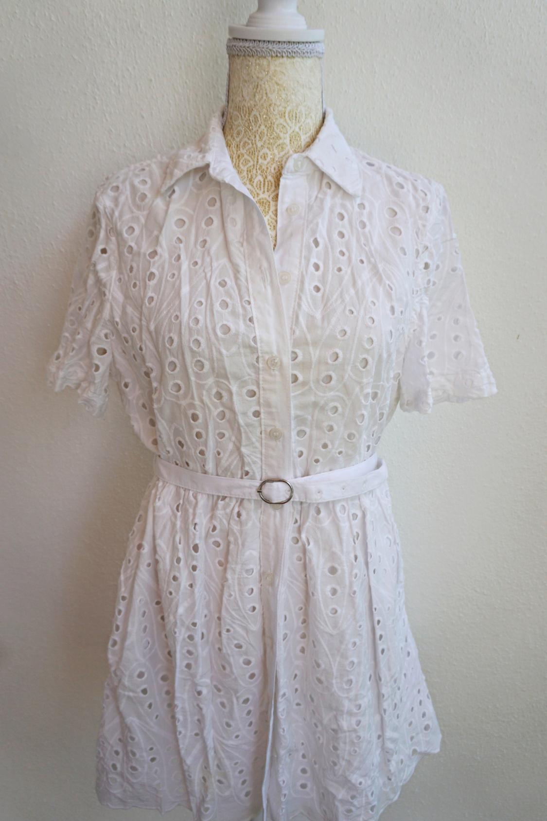 White lace dress with a circular design, short sleeves, and a slim belt. Displayed on a mannequin against a light background.