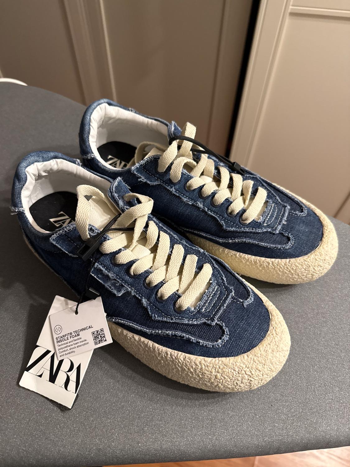 Blue canvas sneakers with a beige sole and white laces on a gray surface. Visible label with text: "ZARA".