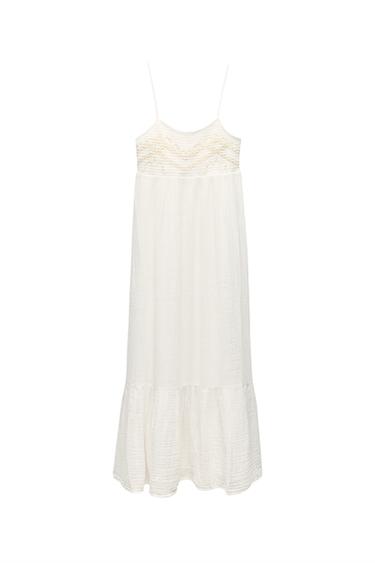 Front view of a long white dress with spaghetti straps and embroidery detail on the chest.