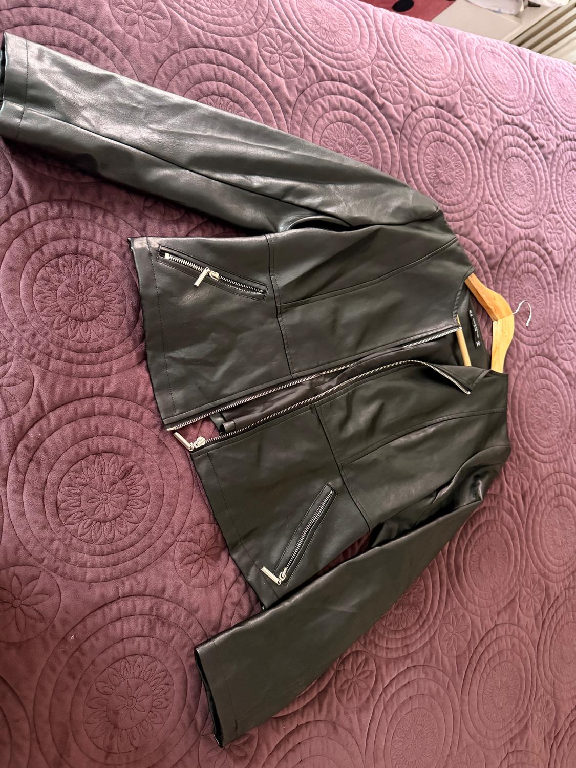 Black leather jacket with silver zippers, placed on a purple comforter with an embossed circle design.