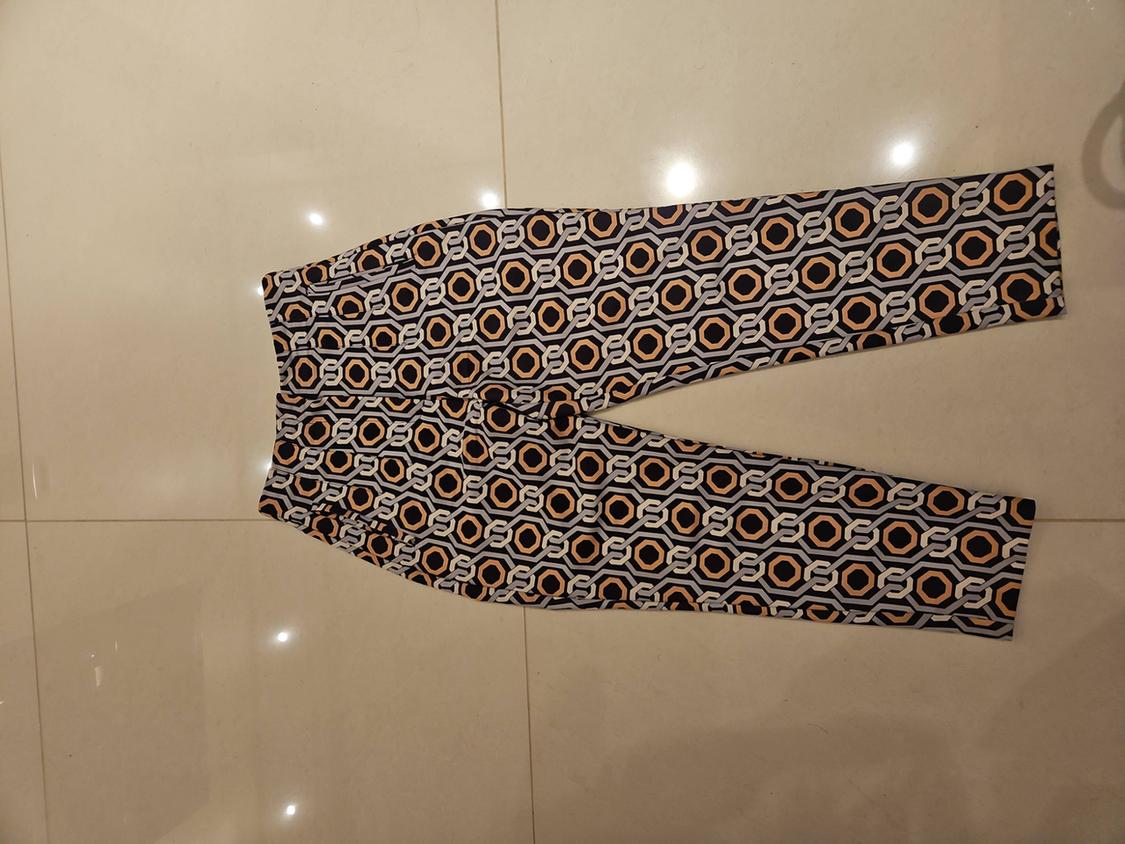 Trousers with a geometric print in black, white, and orange, placed on a shiny beige floor.