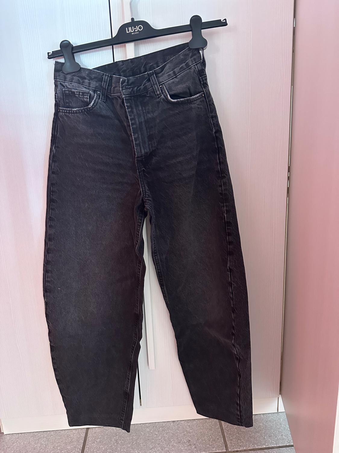 Black washed jeans hanging on a hanger with the text LIU·JO MILANO, in front of a white wardrobe in a casual setting.