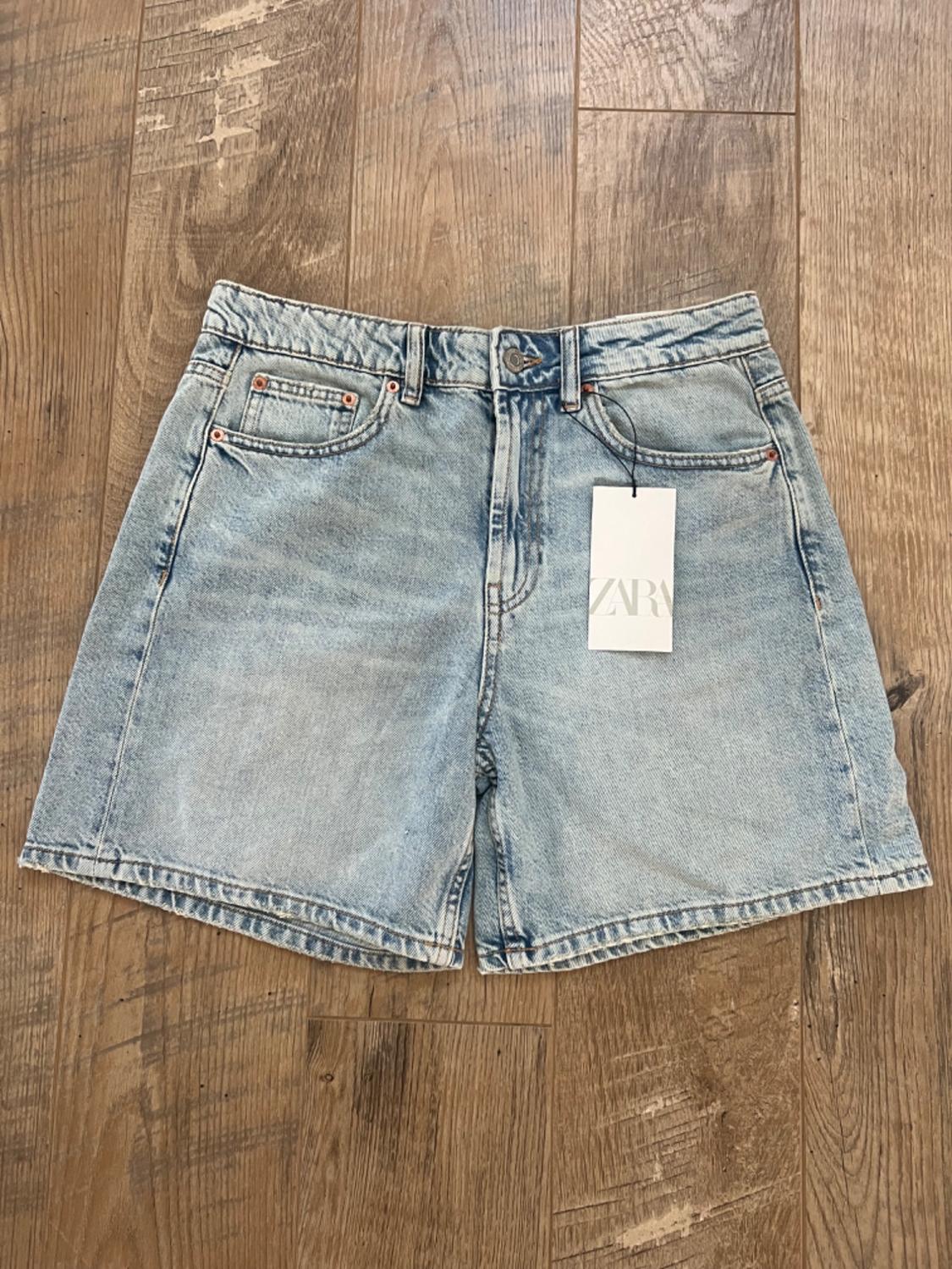 Light blue denim shorts on a wooden floor. Visible label with the text "ZARA".