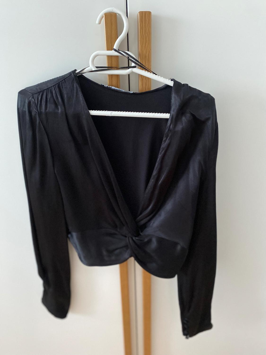 Black long-sleeved blouse with front knot hanging on a white hanger against a light background.