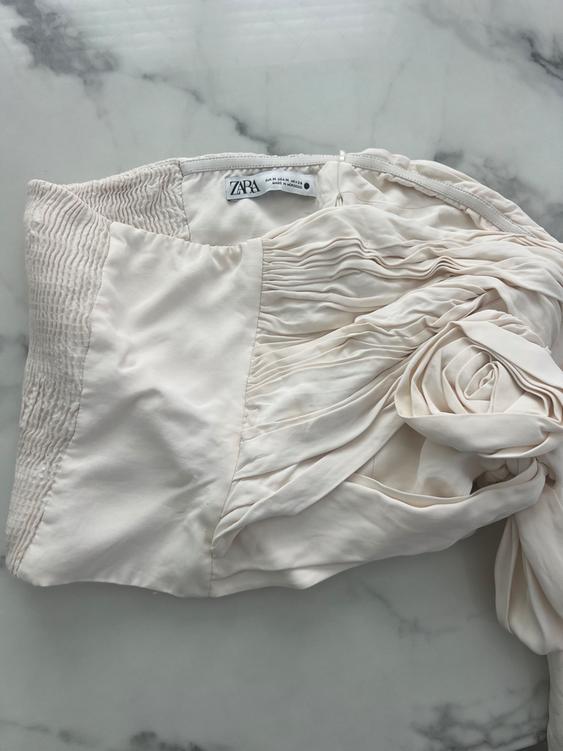 Cream-colored fabric with folds and wrinkled texture on a marble surface. Visible label with the text "ZARA".