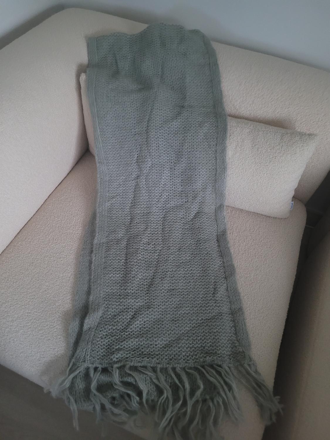 Grey knitted scarf with fringed ends, placed on a beige sofa in the corner of the room.