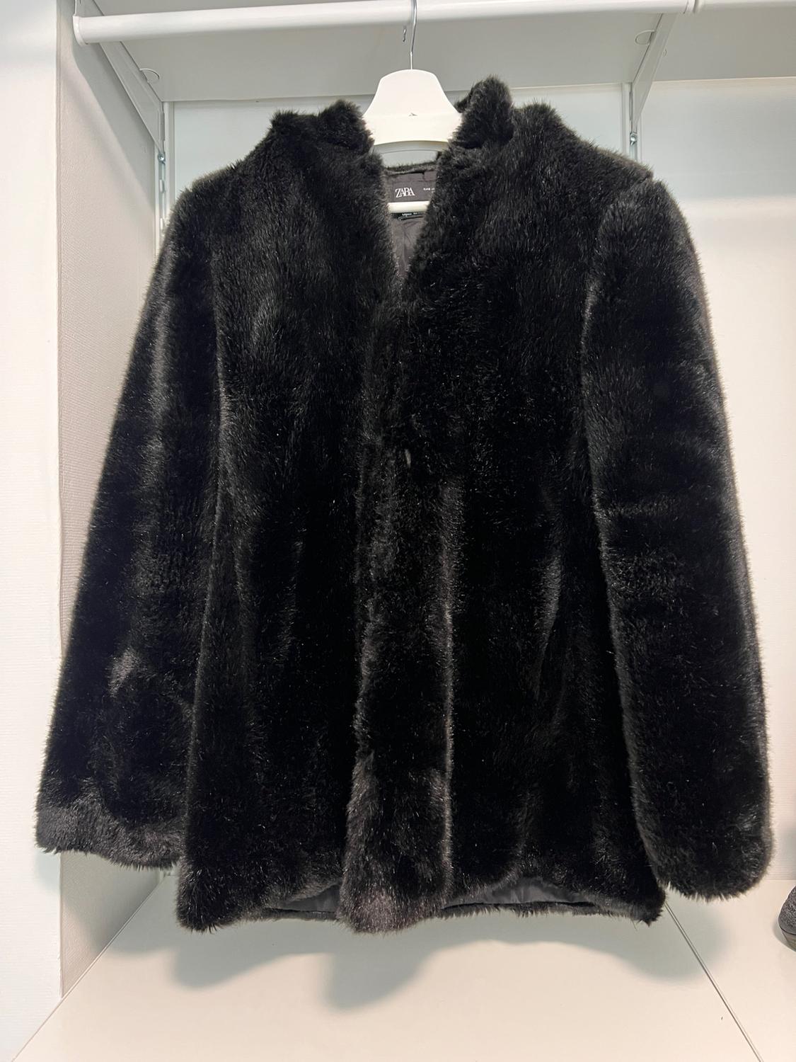 Black faux fur coat hanging on a white hanger in a wardrobe. Visible label with the brand.