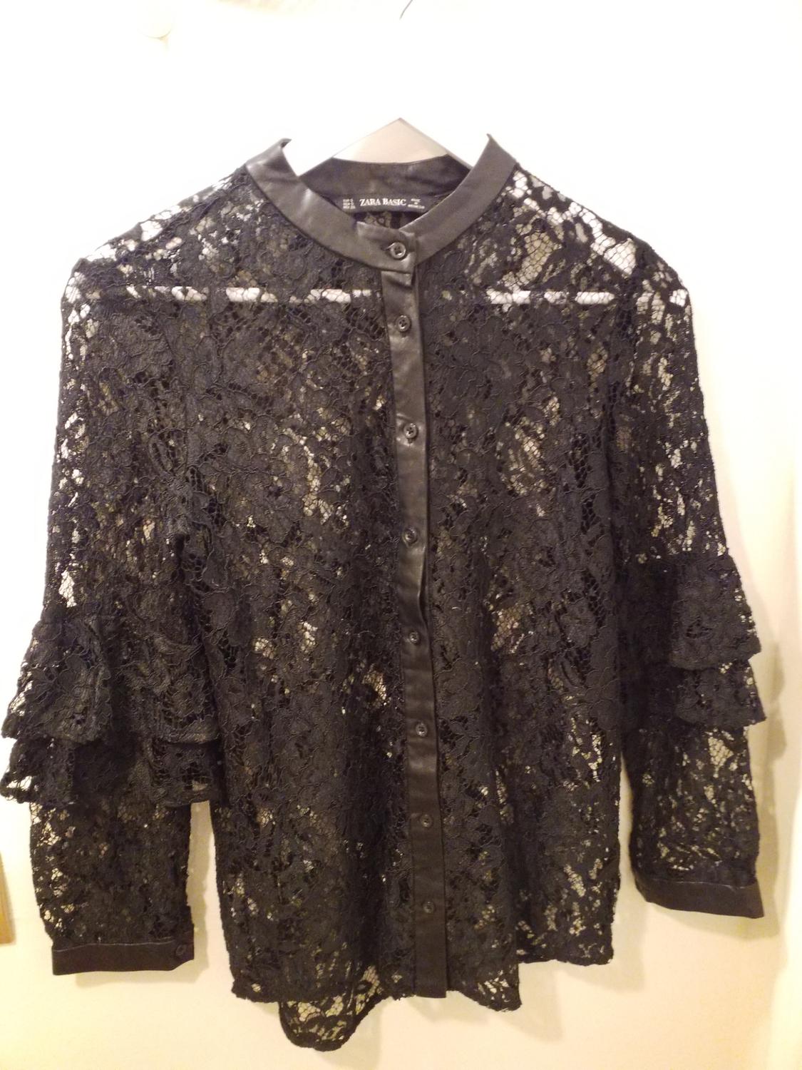 Black lace blouse with buttons and a round neck, hanging on a hanger. Visible label: "Zara Basic". White background.
