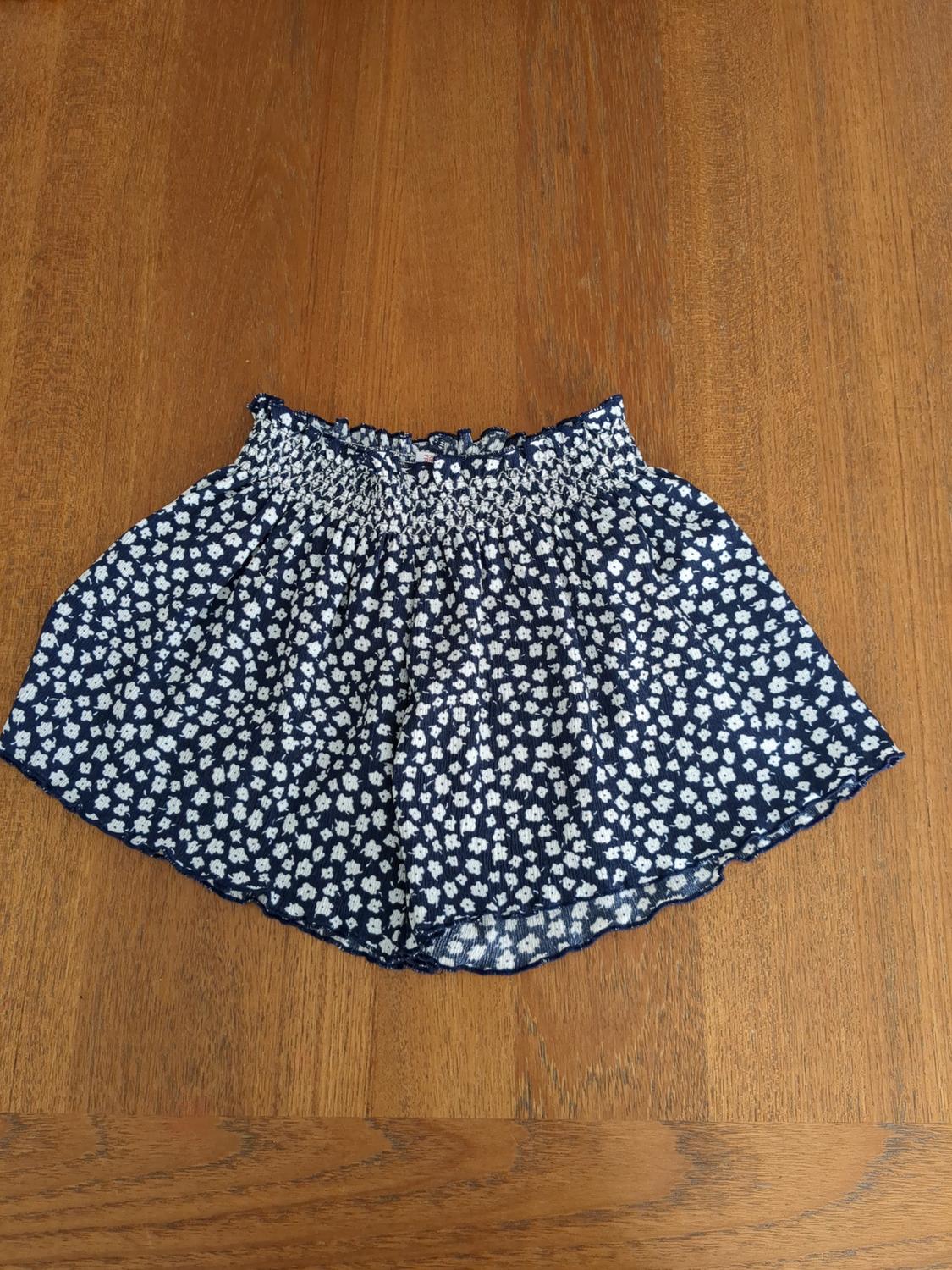 Short blue skirt with a white floral print on a wooden table.