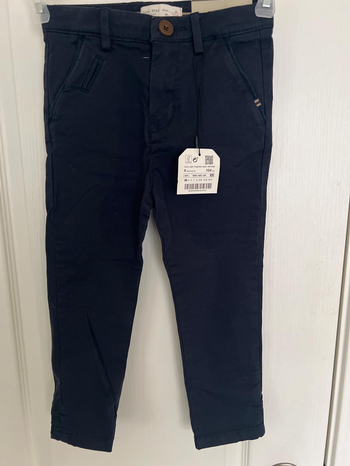Dark blue pants hanging on a white door, with visible price tag. Brown button and side pockets.