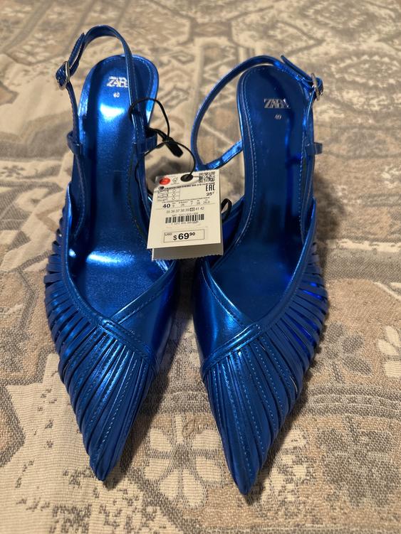 Shiny blue high heels with fringe details and a $69.90 price tag on a patterned surface.