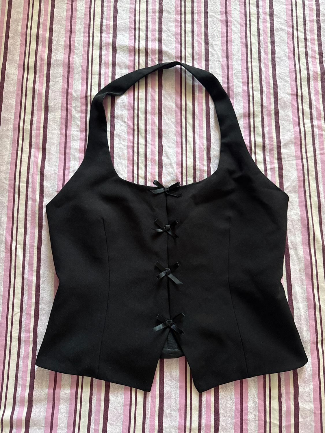 Black halter neck top with four ties at the front, on a background of pink, white, and maroon striped fabric.