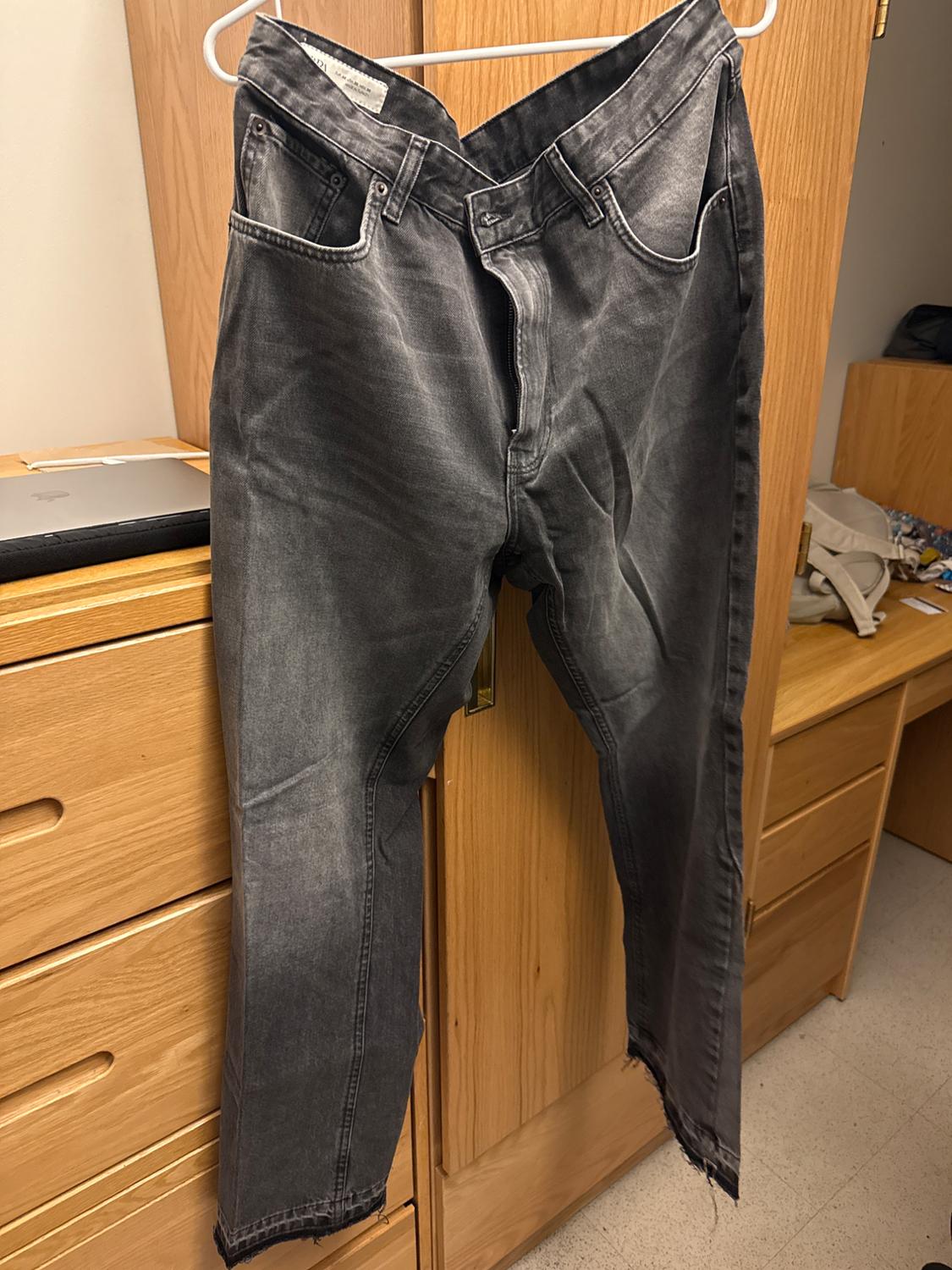 Worn gray jeans hanging on a white hanger over a light wood cabinet. Background with drawers and a laptop.