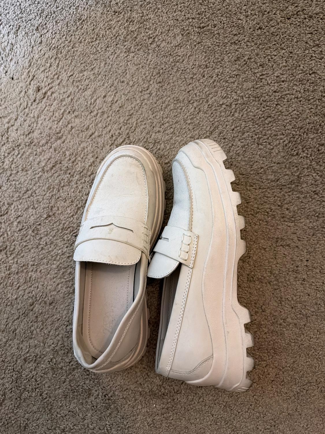 White chunky-soled shoes on a beige carpet. One is on its side showing the sole, the other is viewed from above.