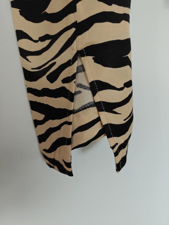 Detail of fabric with black and beige stripe print, showing a slit in the hem over a white background.