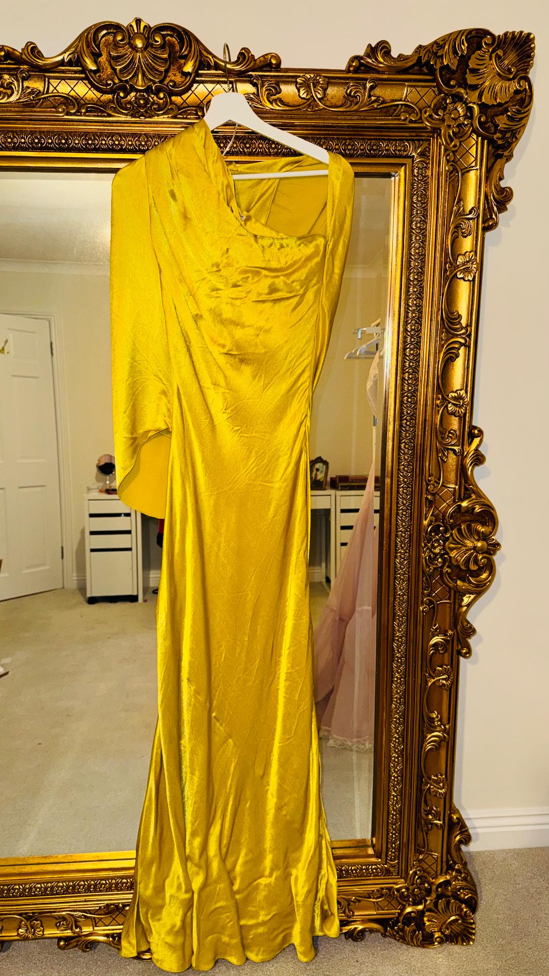 Bright yellow dress hanging on an ornate gold mirror, reflecting a room with white furniture and a beige carpet.