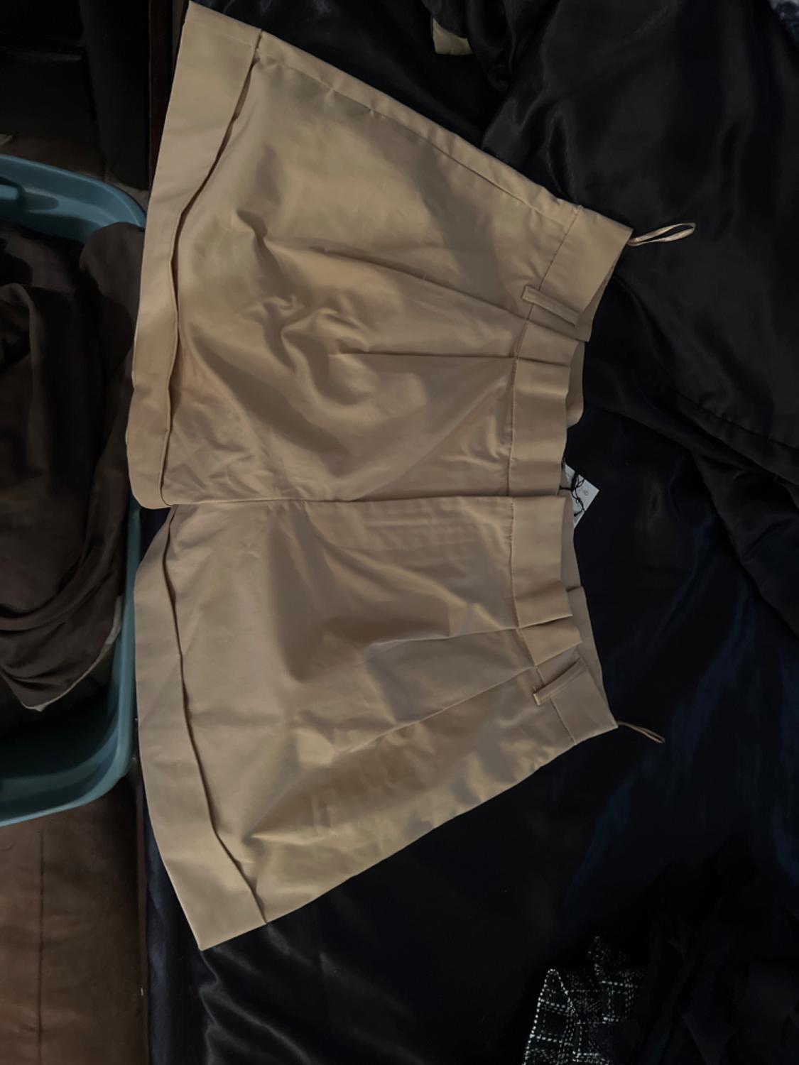 Top view of beige shorts with side pockets and front pleats.