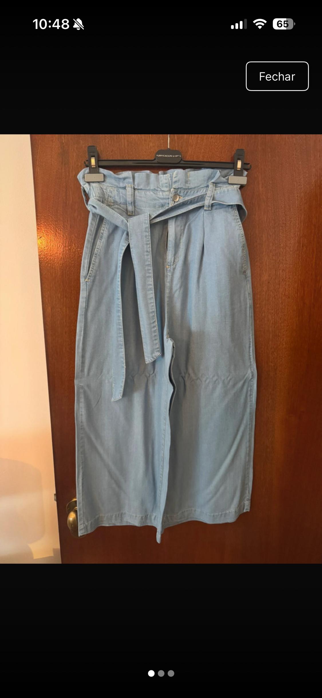 Light blue jeans with a knotted belt, hanging on a wooden door. Text: 10:48, 65, Close, PURIFICACION GARCIA.