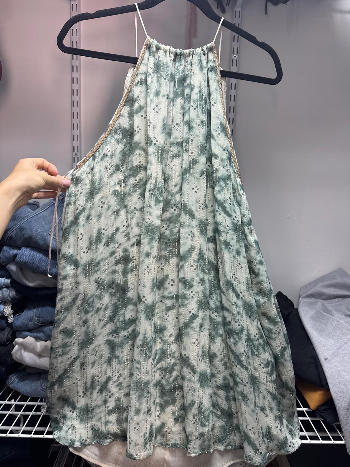 Sleeveless green dress with a tie-dye print and sequin detailing, hanging on a black hanger on a clothes rail.