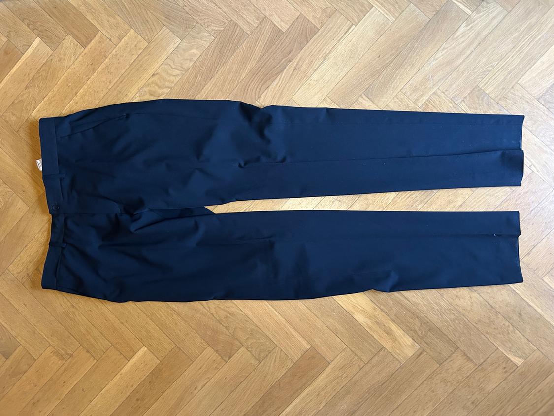 Dark dress trousers laid out on a herringbone wooden floor. Relaxed style, top view.