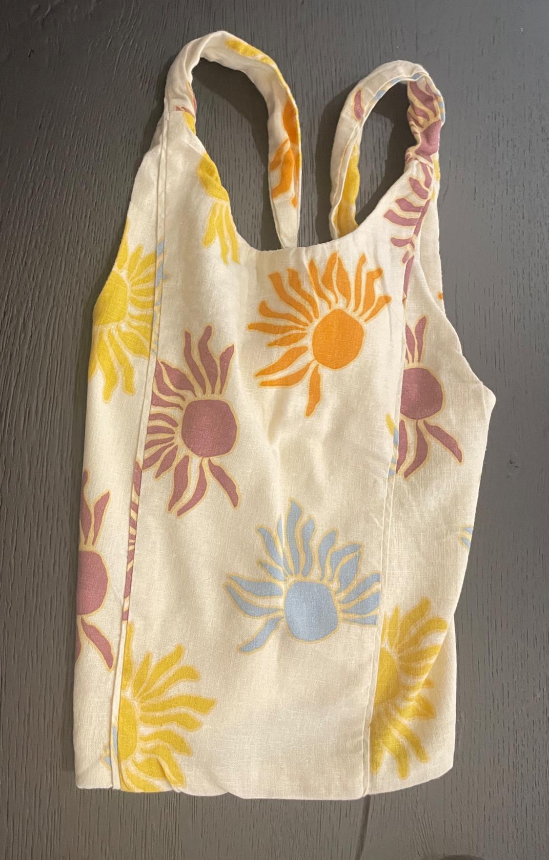 White sleeveless top with sun print in yellow, orange, pink and blue, on a grey wooden surface.