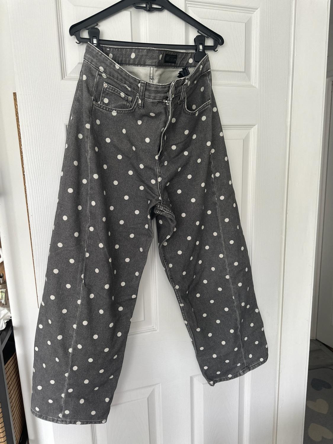 Grey wide-leg jeans with a white polka dot print,
hanging on a black hanger on a white door.