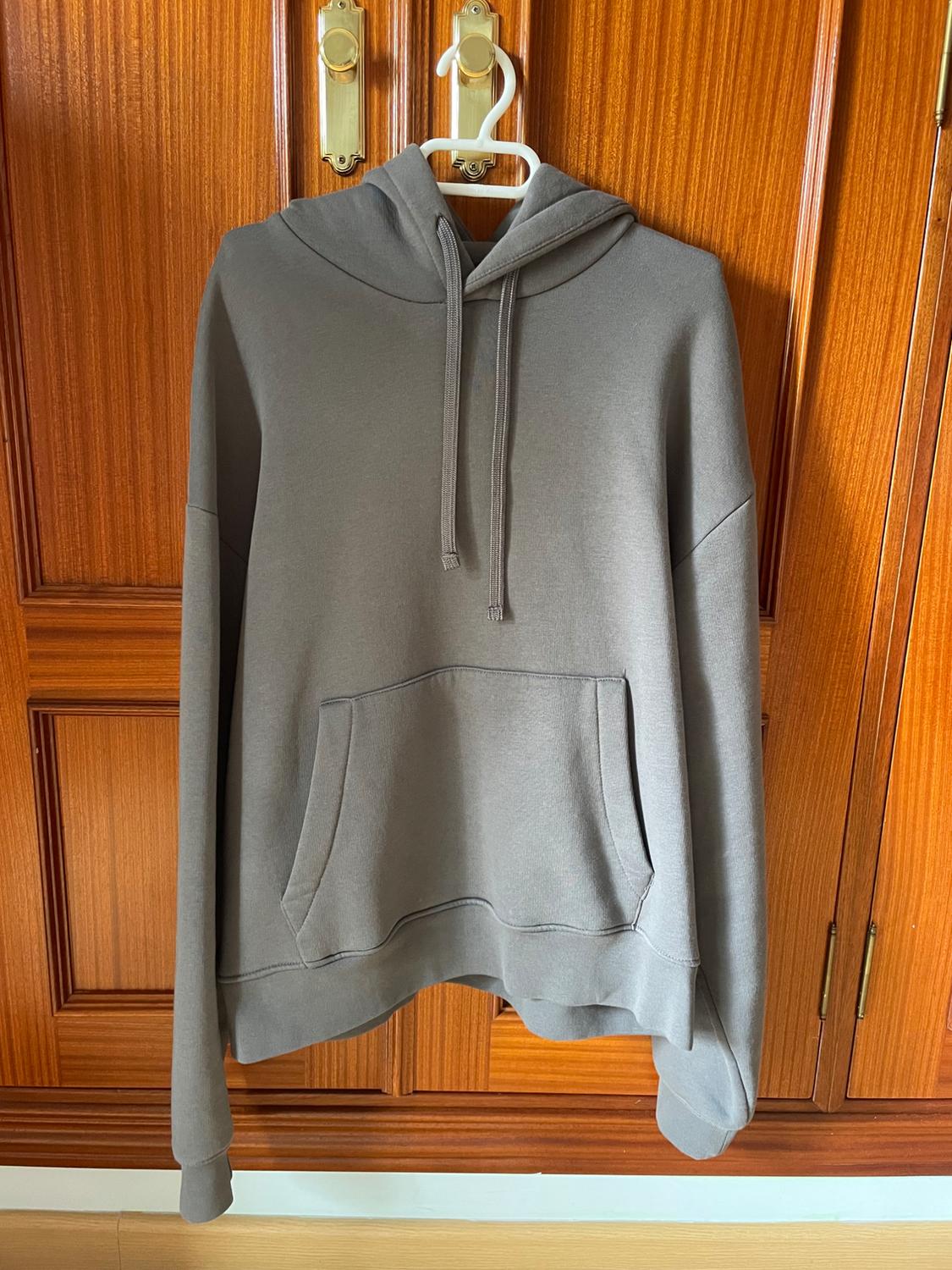 Grey hoodie with a front pocket hanging on a white hanger on a brown wooden door.