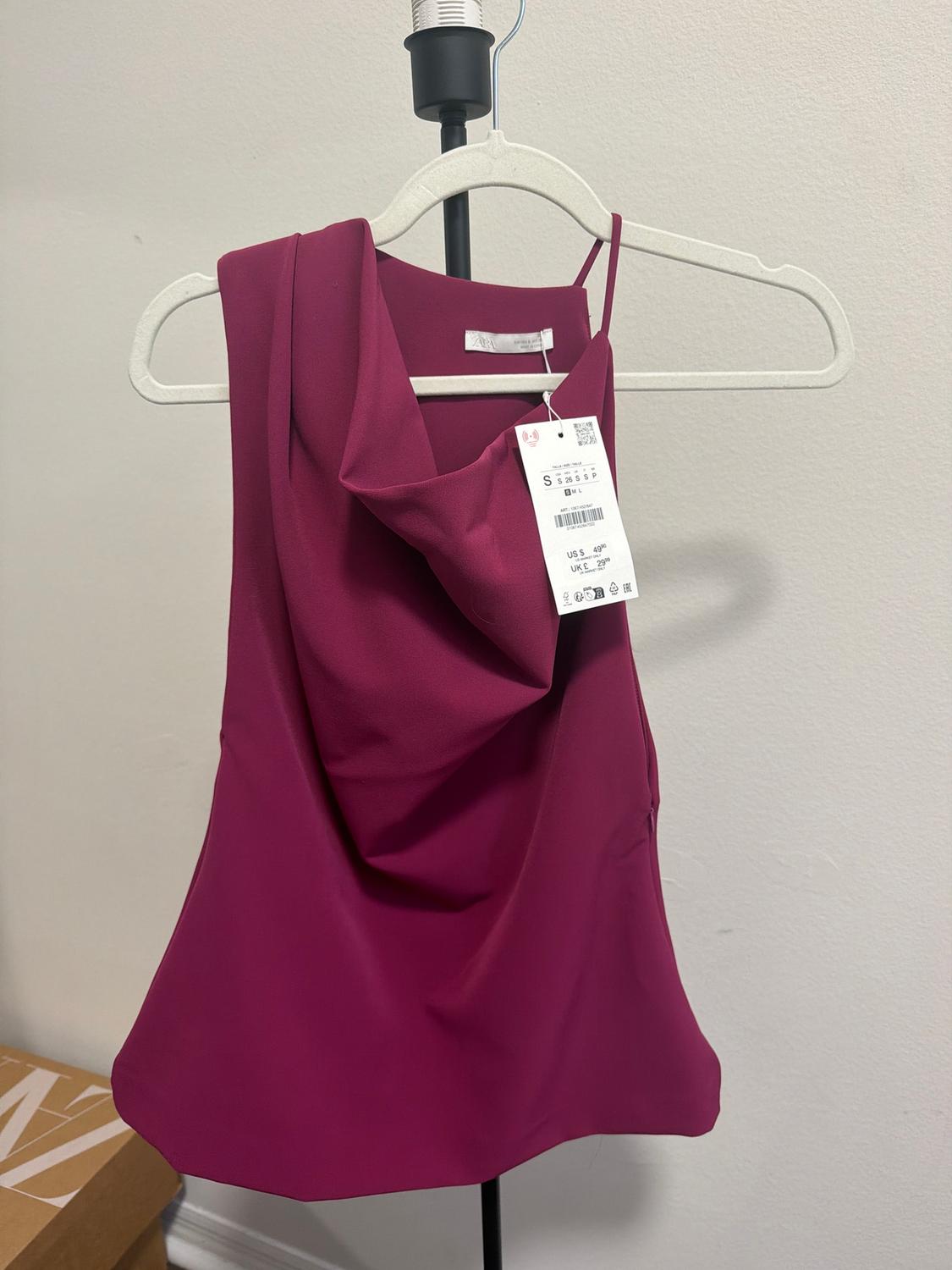 Fuchsia sleeveless blouse with a draped neckline on a white hanger. Visible tag with size and price details. White background.
