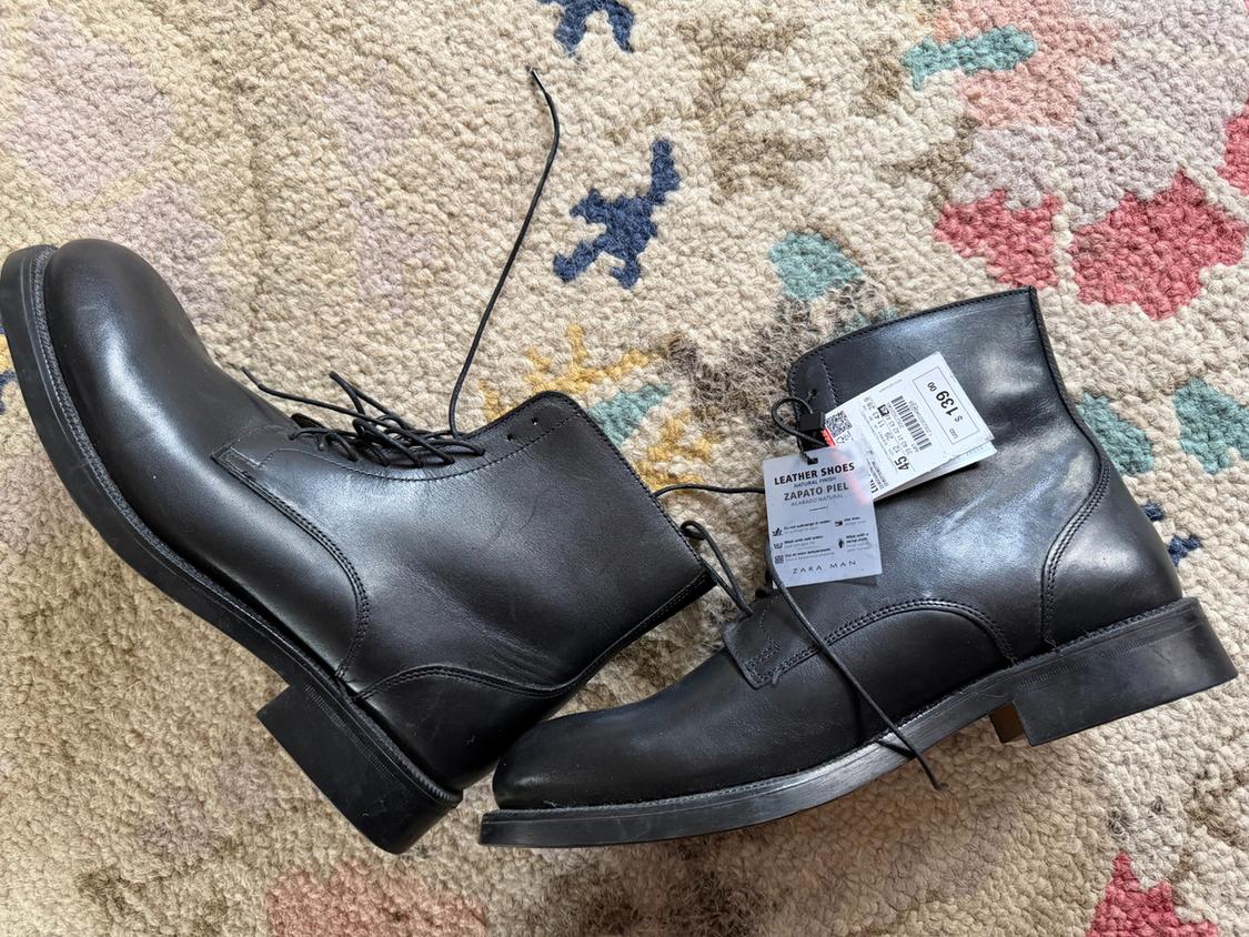 Black leather lace-up boots on a colourful rug. Visible tags: "LEATHER SHOES", "LEATHER SHOE", "ZARA MAN", price $1399.