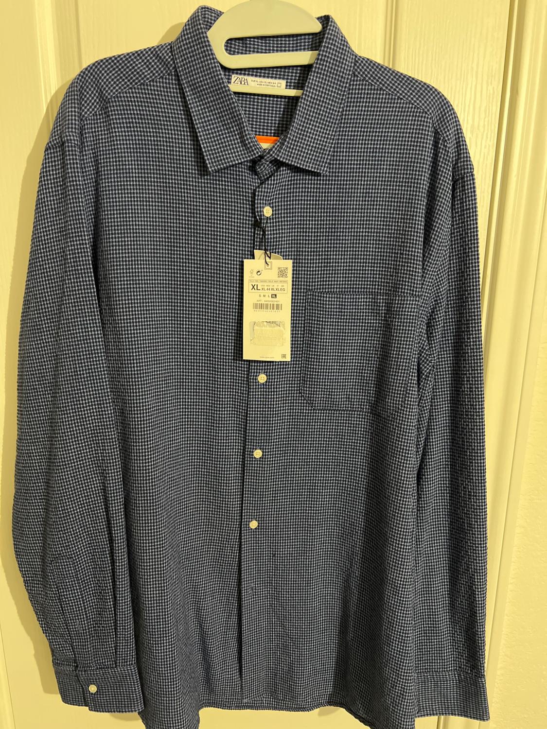 Small plaid shirt in dark tones hanging on a hanger. Visible tag with XL size details and barcode.