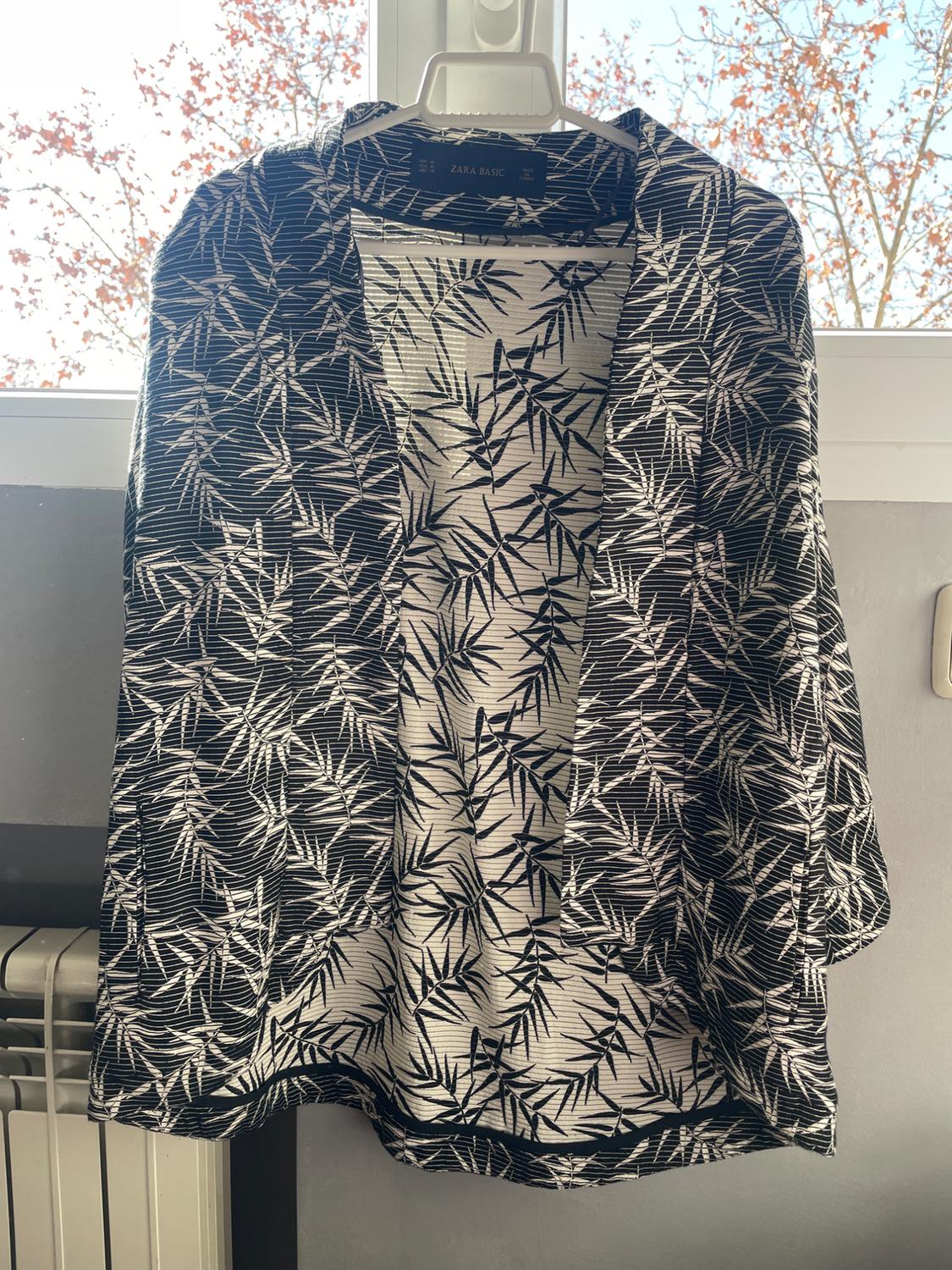 Front view of a black and white leaf-print jacket hanging on a hanger.
