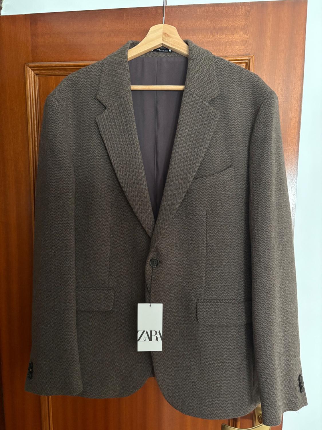 Brown wool jacket with a herringbone pattern hanging on a wooden hanger. Label visible with the text "ZARA".