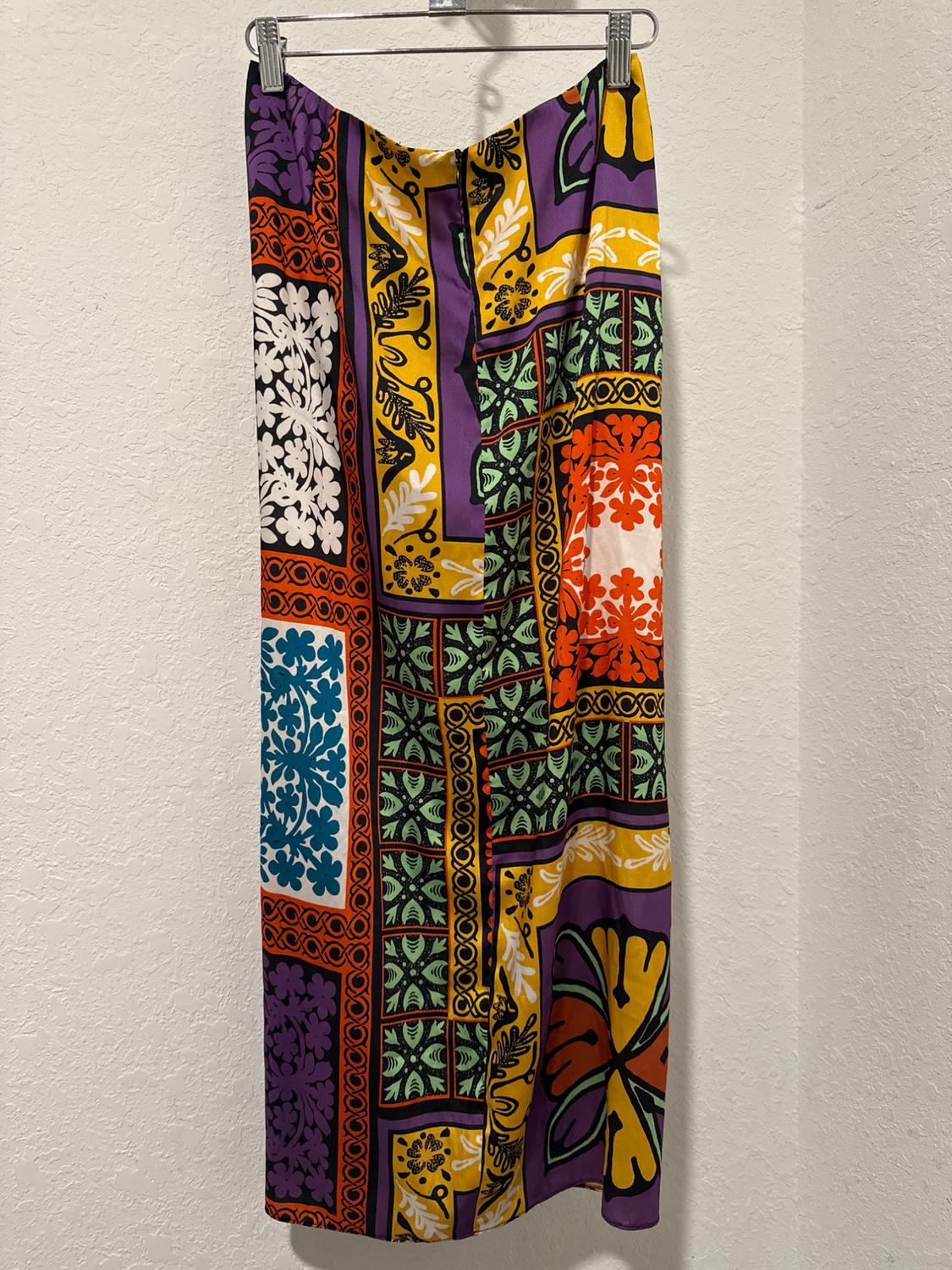 Long skirt with a geometric and floral print in vibrant colours like purple, yellow, green, and orange, hanging on a hanger.