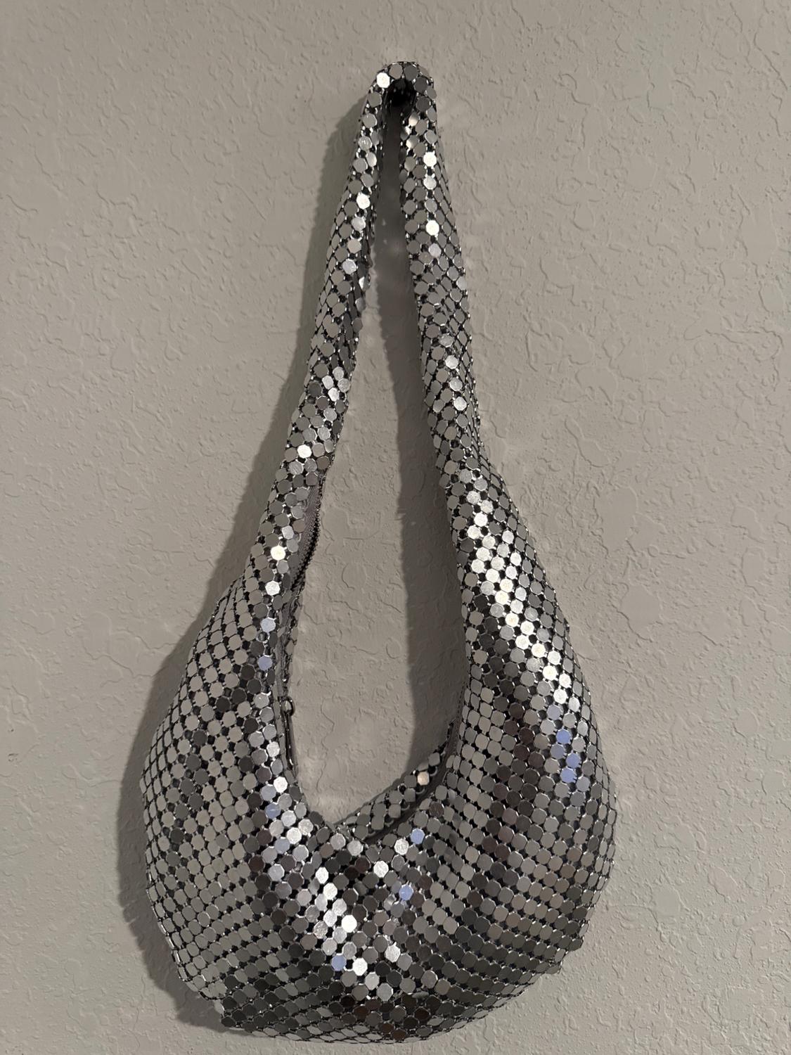 Silver sequined handbag hanging on a grey textured wall. Bright and modern design, ideal for special occasions.