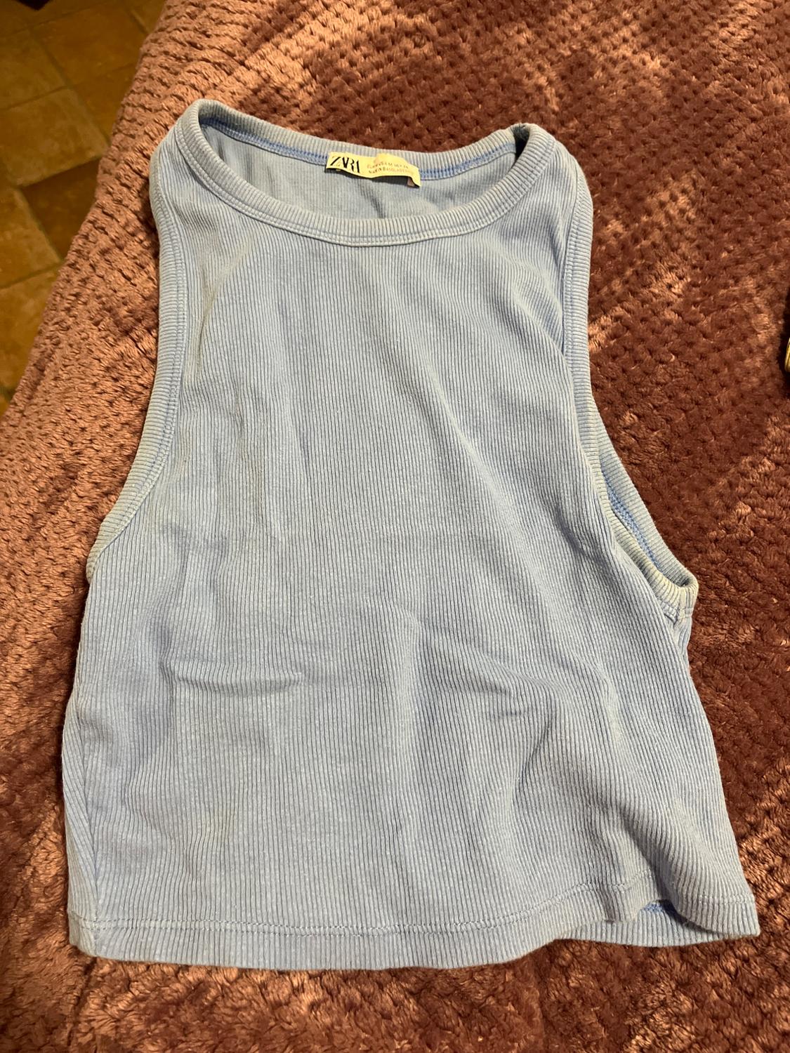 Light blue ribbed vest top on a brown blanket. Visible neck label with text "ZV1".