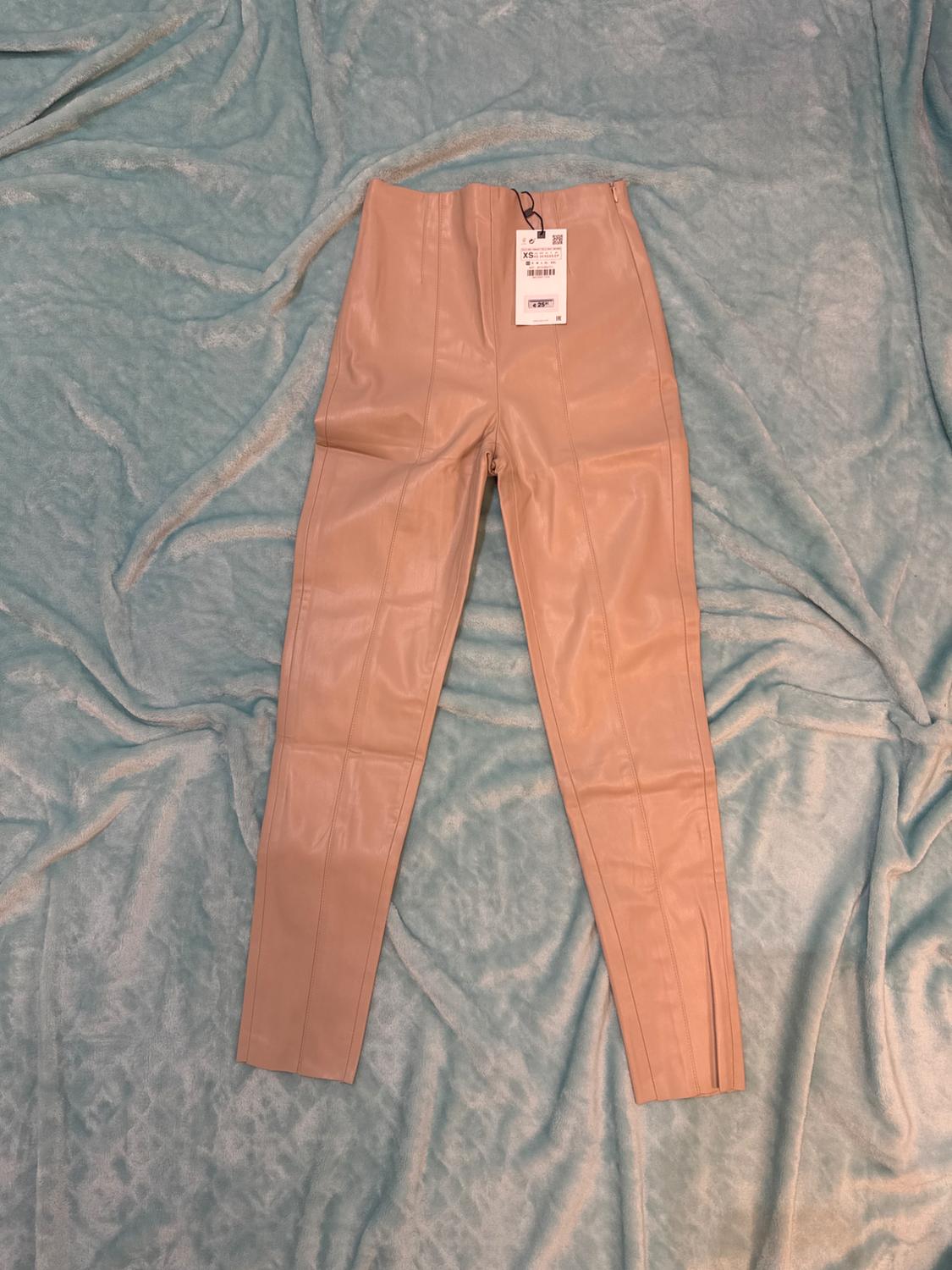 High-waisted beige trousers on light blue fabric, with visible hang tag at the top centre.
