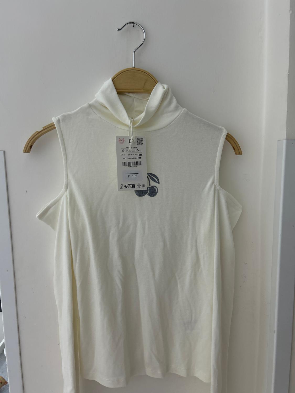White sleeveless hooded top hanging on a wooden hanger. Visible product details label. White background.