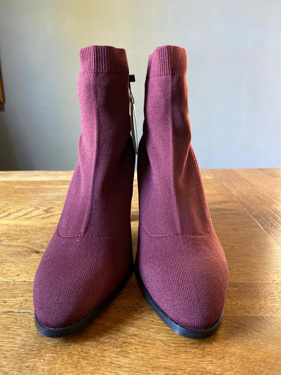 Burgundy knitted ankle boots with a pointed toe, presented on a wooden table
with a neutral background.
