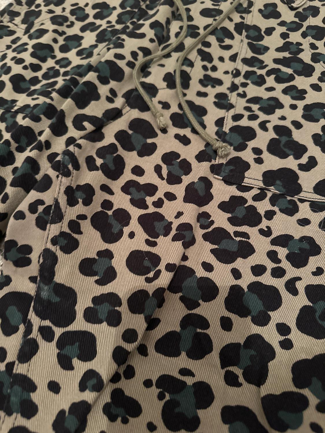 Fabric with a black and green spot print on a beige background, with visible green drawstrings at the top.