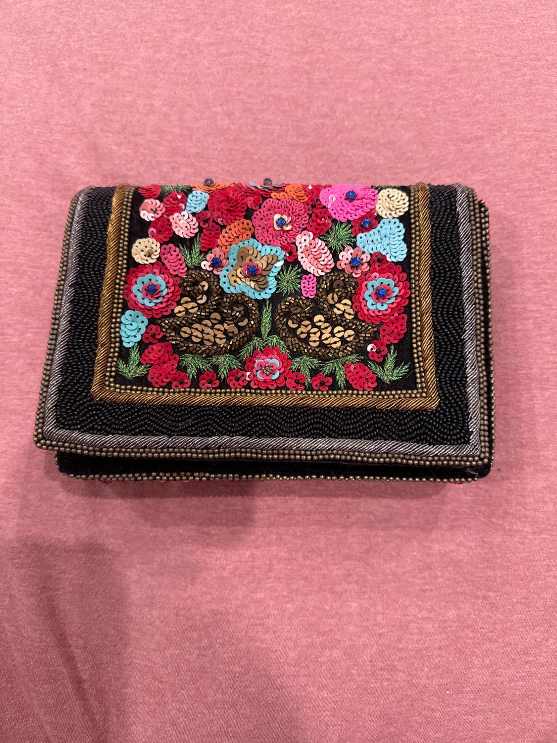 Wallet embroidered with coloured sequins and a floral design on a black background, placed on pink fabric.