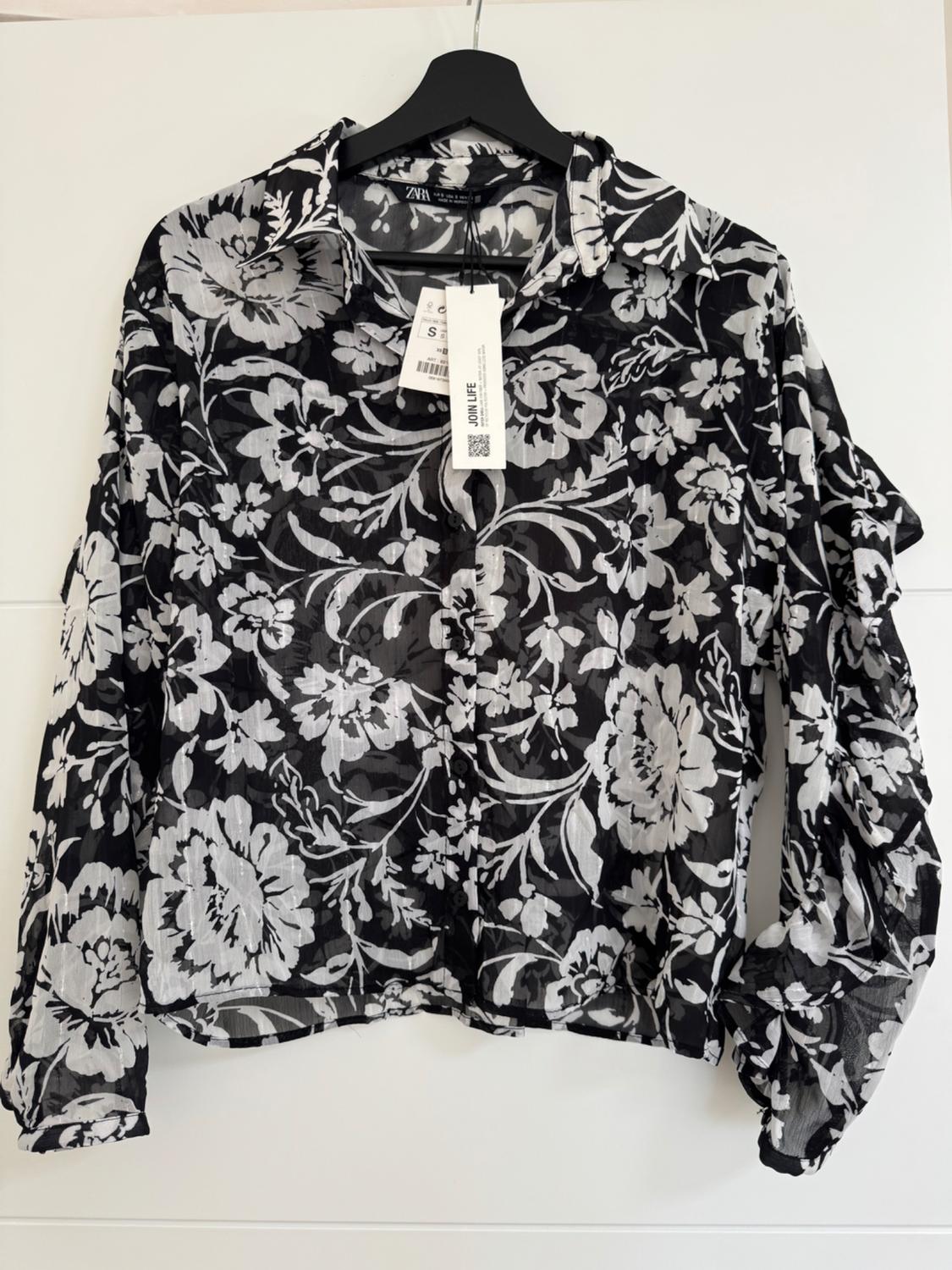 Sheer black and white floral print blouse, hanging on a black hanger. Visible label with text "JOIN LIFE".