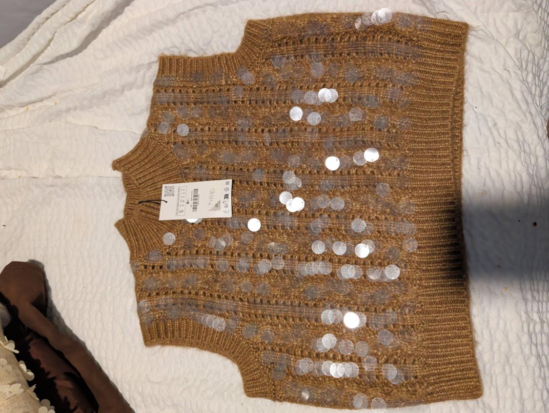 Brown vest with silver sequins on a white quilt. Visible tag with product details.