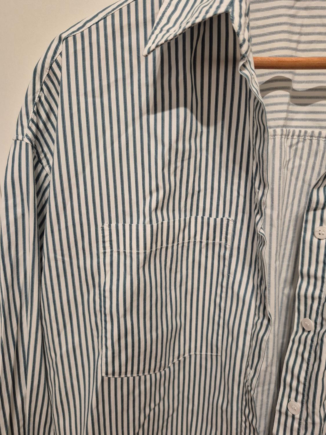 Blue and white vertically striped shirt hanging on a wooden hanger. Pocket detail and buttons visible.