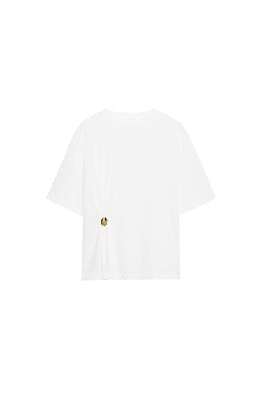 Front view of a ripped white T-shirt, short-sleeved, round neck, straight hem, with a metallic appliqué on the side.