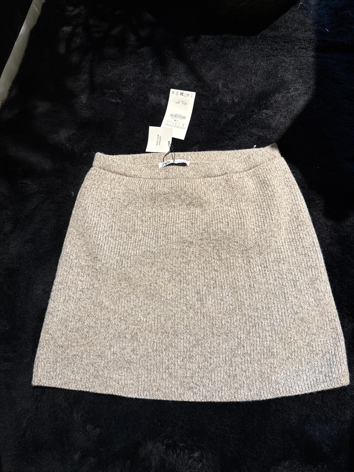Gray knit mini skirt on a black background, with visible tags at the top.