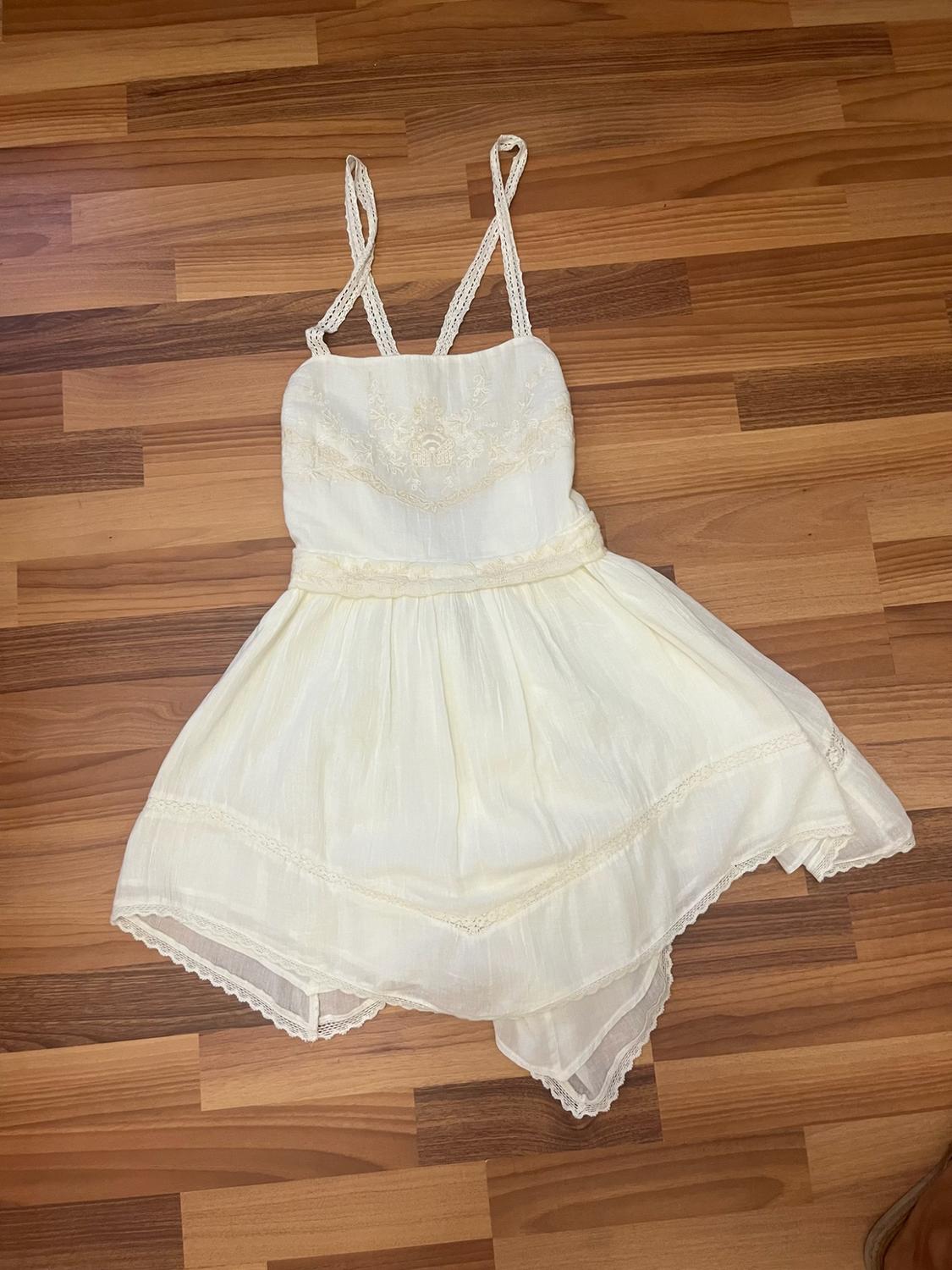 White camisole dress with embroidery on the chest and an asymmetric skirt with lace detailing, laid out on a wooden floor.